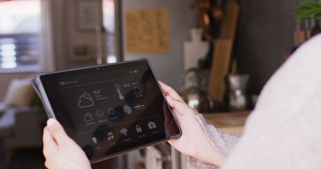 Hands holding tablet displaying smart home control interface in contemporary home interior. Ideal for topics on smart home technology, modern households, home automation, IoT devices, and tech-driven lifestyles.