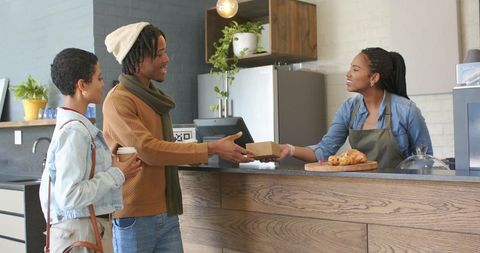 Smiling diverse couple receiving takeaway box from barista in cozy urban coffee shop