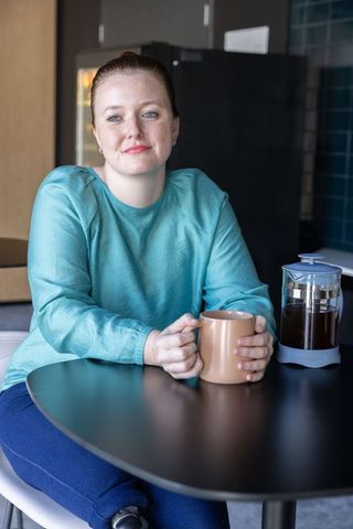 Mid-adult woman relaxing with coffee in office kitchenette