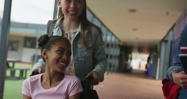 Two Happy Girls in a School Hallway, One Pushing the Other in a Wheelchair - Download Free Stock Images Pikwizard.com