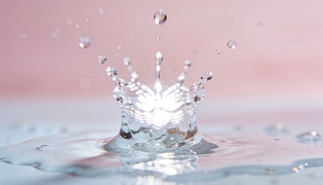 High-speed water crown splash forming on reflective surface with soft pink background