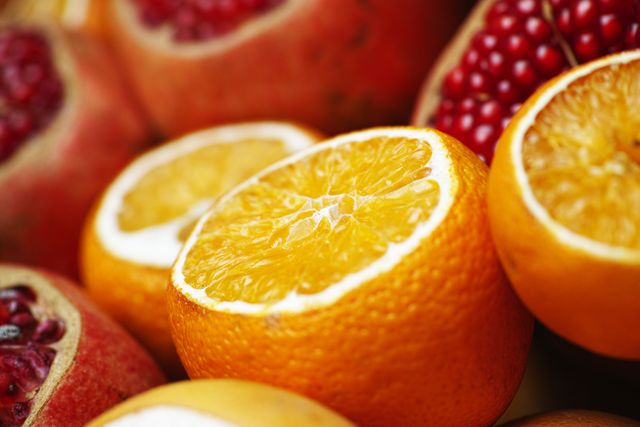 This image shows a close-up view of fresh oranges with one sliced in half revealing its juicy flesh, surrounded by pomegranates. The vibrant colors and refreshing look make it ideal for use in advertisements, health blogs, and publications focused on nutrition and healthy living.