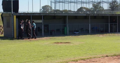Baseball coaches gathering by dugout on sunny grass field, team planning moment