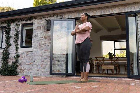 African american woman practicing yoga on patio barefoot with dumbbells and mat