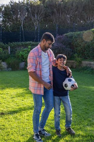 Smiling father and son holding soccer ball outdoors in sunny garden