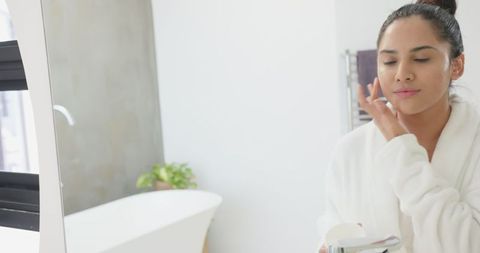 Woman Applying Face Cream for Skincare in Modern Bathroom