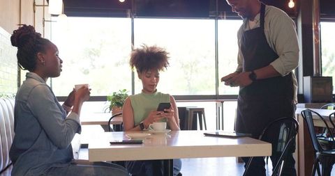 African american friends enjoying coffee and using phones while barista processing order