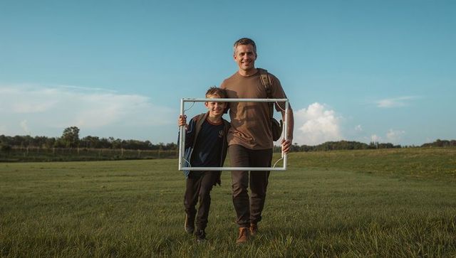 Father and son walking in meadow holding frame, outdoor family bonding