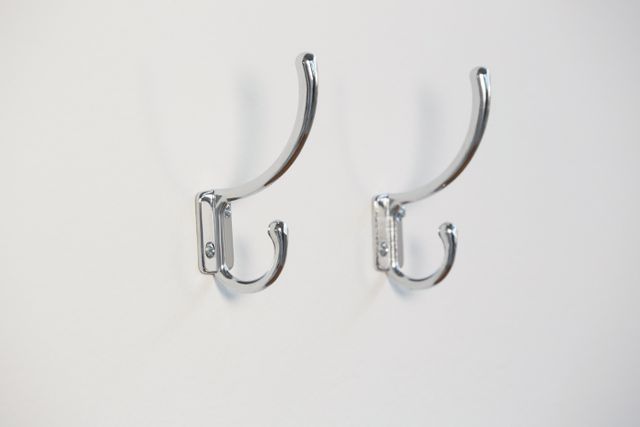 Close-up view of two chrome hooks mounted on a white wall, ideal for home organization and storage solutions. Perfect for use in articles or advertisements about interior design, minimalist decor, or practical home storage ideas.