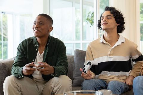 Diverse young men playing video games on couch in bright contemporary living room