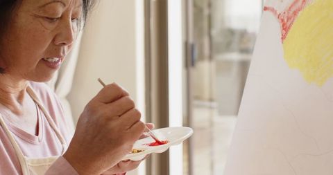 Senior Asian Woman Painting on Canvas in Home Art Studio