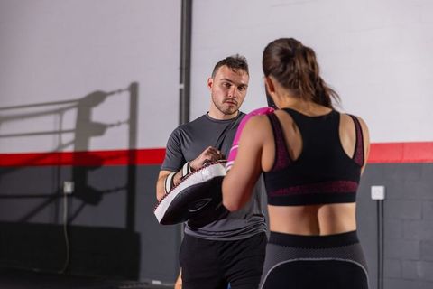 Female boxer training with coach holding focus pad, wearing pink gloves in boxing gym