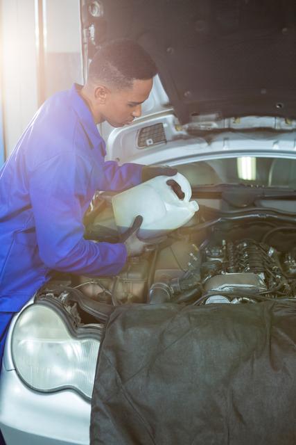 Mechanic pouring oil lubricant into the car engine at garage