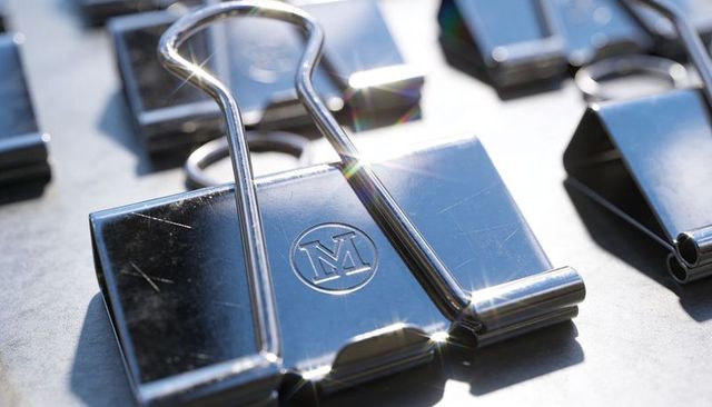 Shining chrome binder clip with embossed m logo, macro metal office fastener close-up