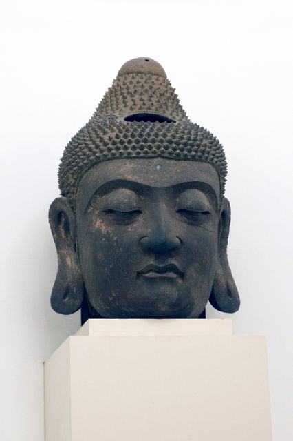 Depicting a Buddha head sculpture with a serene expression, evoking a sense of peace and spirituality. This ancient stone artwork showcases intricate details and a timeless, meditative aura, suitable for use in historical documentaries, educational materials, spiritual or religious publications, and Asian art exhibitions.