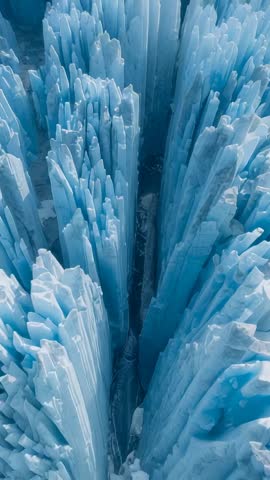Vertical Drone Descent Through Blue Ice Canyon Revealing Frost-Covered Glacier Pillars