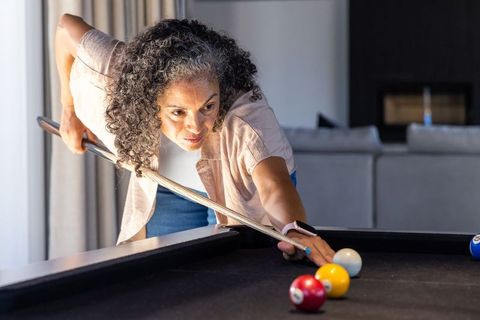 Senior african american woman playing pool at home concentrating on precision shot