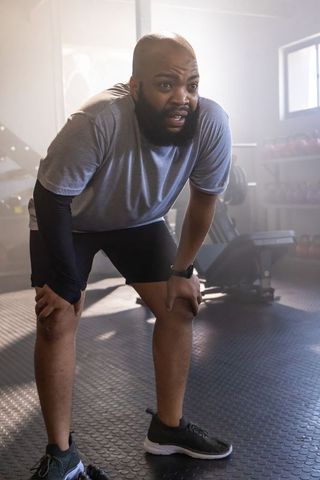 African american man catching breath after intense workout in gym, recovering between sets