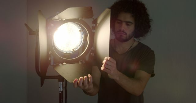 A young Caucasian man adjusts a large studio light, with copy space. His focused expression and the lighting equipment suggest he is a professional working in film or photography.