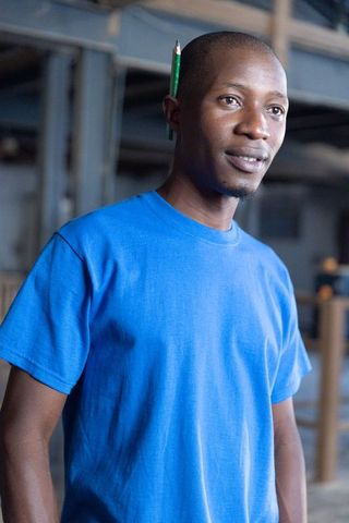 African american craftsman wearing blue shirt with pencil behind ear in workshop