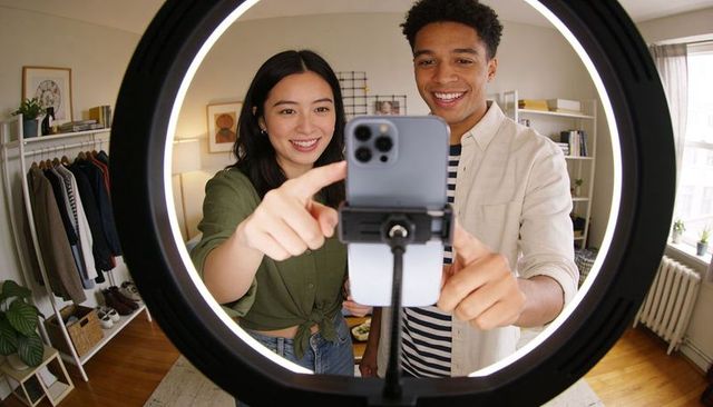 Young couple creating fashion content with smartphone and ring light in cozy home studio