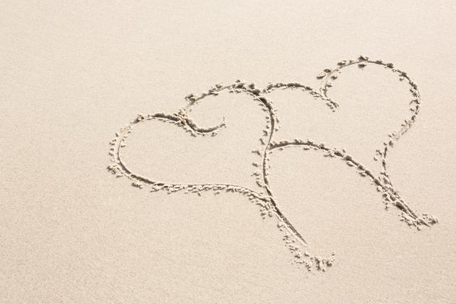 Two heart shapes drawn on sand on beach