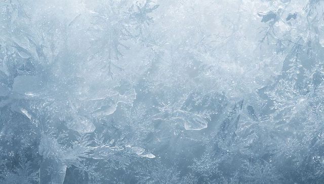 Macro frost crystals forming intricate dendritic ice patterns on translucent blue glass