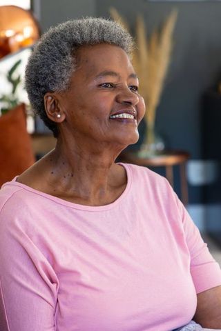 Senior african american woman smiling and sitting in cozy living room wearing pink top