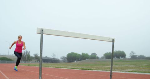 Female Athlete Training on Track Jumping Hurdle
