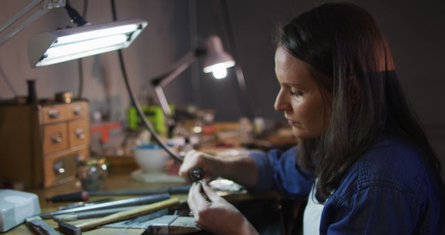 Focused caucasian female jeweller sitting at desk, making jewelry in workshop - Download Free Stock Photos Pikwizard.com