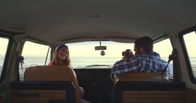 Couple savoring beach view from the interior of a vintage van. Man capturing view with camera, woman smiling. Ideal for travel blogs, adventure promotions, vacation brochures, photography sessions, and lifestyle campaigns.