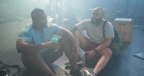 Two men resting after training beside translucent shaker bottle and plyo box in gym