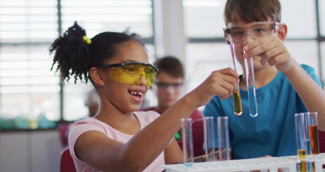 Young students actively engaged in a science experiment with test tubes in a classroom setting. They are wearing protective eyewear while holding test tubes with colorful liquids. This image is ideal for educational content, science-related articles, promotional materials for STEM programs, school brochures, and any materials encouraging hands-on learning.