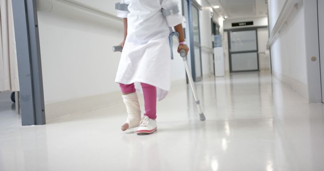 Midsection of african american girl patient with crutches walking in corridor in hospital. Medicine, healthcare and hospital.