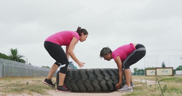 Diverse female friends cross training outdoors, lifting truck tyre. Female fitness, challenge and healthy lifestyle.