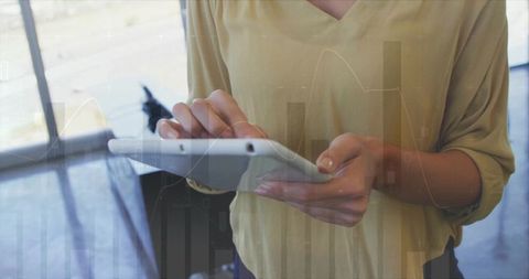 Female Using Tablet for Data Analytics in Modern Office with Financial Graph Overlay