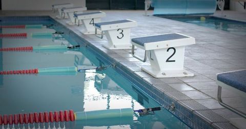 Starting blocks lined at indoor competition pool with lane ropes and water reflections