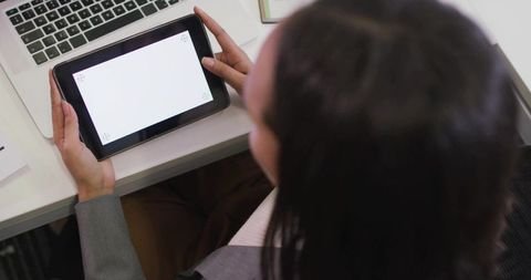 Professional woman holding tablet with blank screen at modern office desk, back view