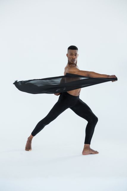 Male ballerino performing ballet dance routine in studio setting. Dressed in black tights, dancer showcases flexibility and grace. Perfect for use in advertisements, dance school promotions, performing arts brochures, and articles on ballet or fitness.