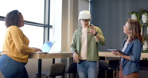 Diverse team testing virtual reality headset while collaborating around modern high table