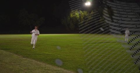 Night cricket player running across floodlit outfield with netting foreground