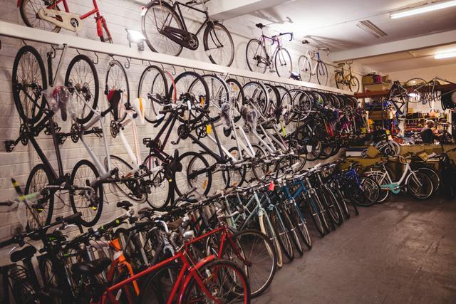 Bicycle workshop filled with various types of bicycles hanging on walls and standing on the floor. Ideal for use in articles about cycling, bike maintenance, bicycle repair shops, or sports equipment stores. Can also be used in advertisements for bicycle shops or cycling gear.