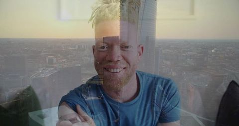 Smiling blond dreadlocked man with beard leaning by window with cityscape double exposure