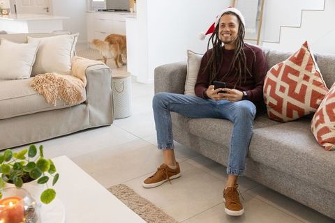 African american man relaxing on sofa wearing santa hat in modern cozy living room