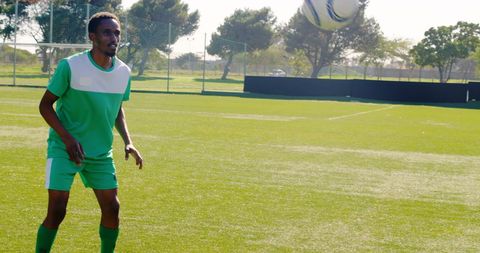 African american man playing soccer in sunlit park