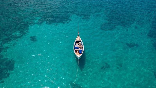 Aerial small wooden boat floating on crystal turquoise water with tethered anchor line