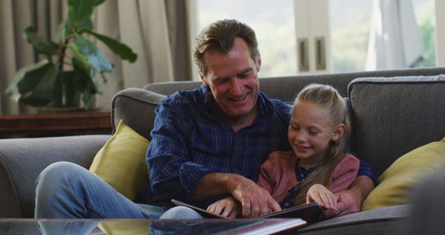 Smiling Grandfather Reading with Granddaughter on Couch at Home - Download Free Stock Images Pikwizard.com