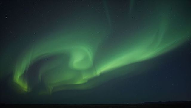 Aurora Borealis swirling green curtains over tundra and silhouetted hills under starry sky