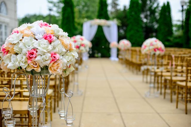This image captures a beautiful outdoor wedding aisle adorned with intricate floral arrangements, elegant chairs, and a decorated arch. Perfect for ads, websites, and blog posts related to wedding planning, bridal events, or celebration inspirations.