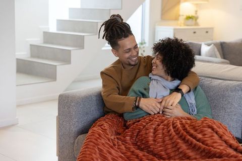 African american couple cuddling on sofa under rust blanket in cozy modern living room